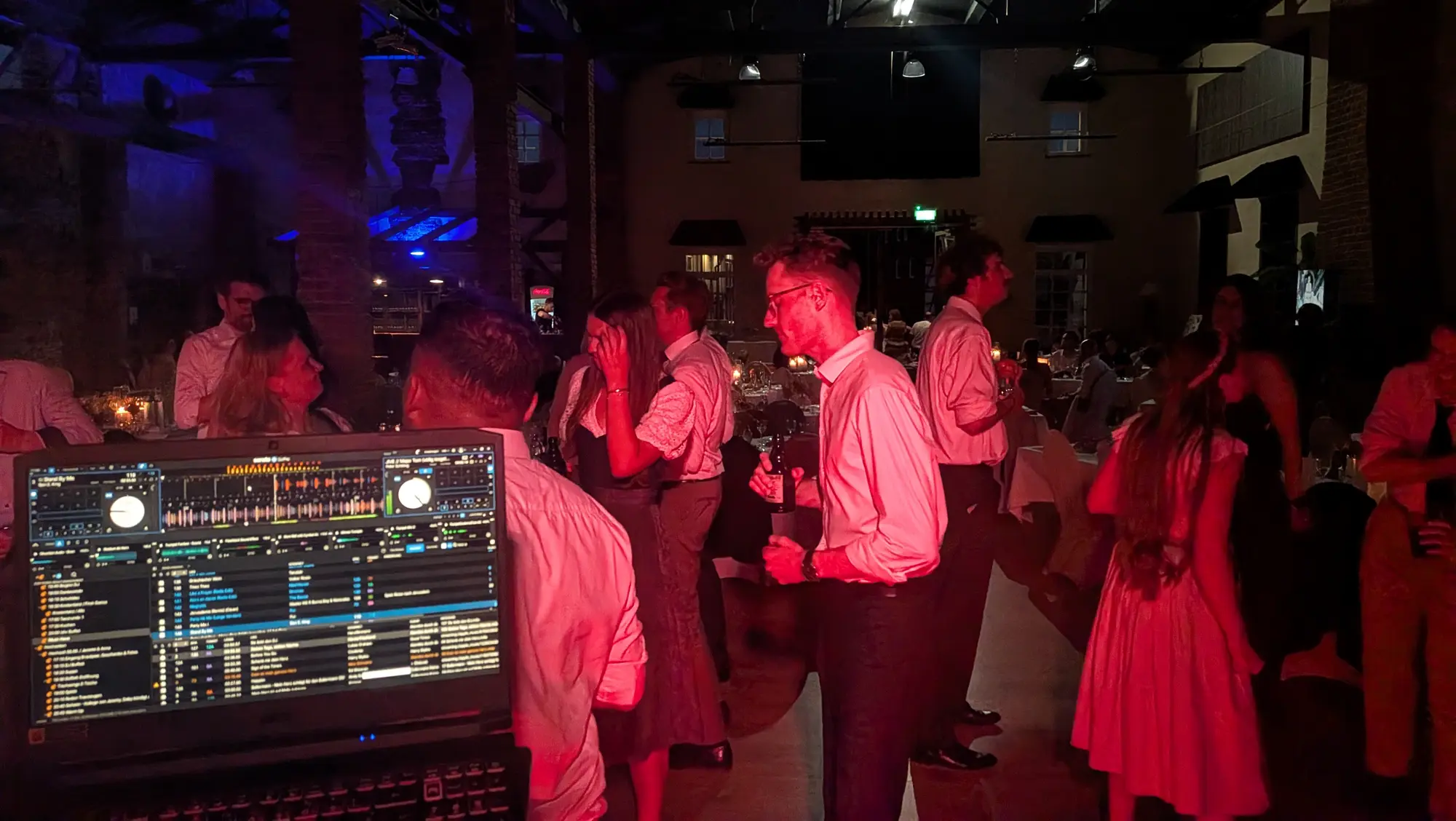 Hochzeitsgesellschaft im warmen roten Partylicht neben dem DJ-Pult
